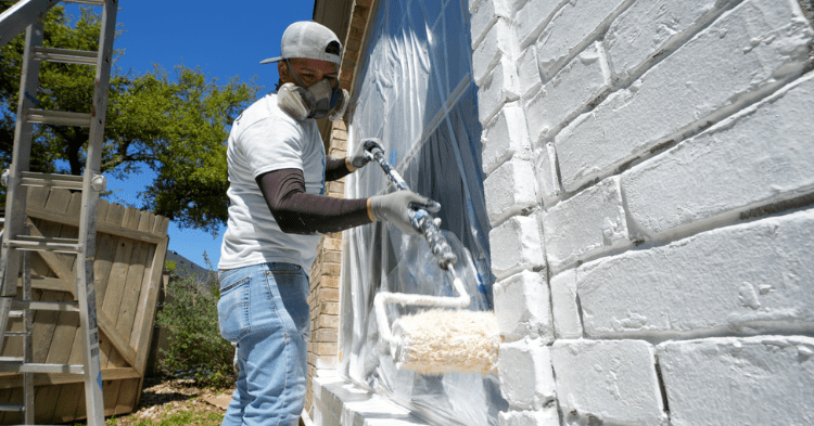 a professional painter using a roller to apply white paint on a brick home_That 1 Painter Arlington Alexandria