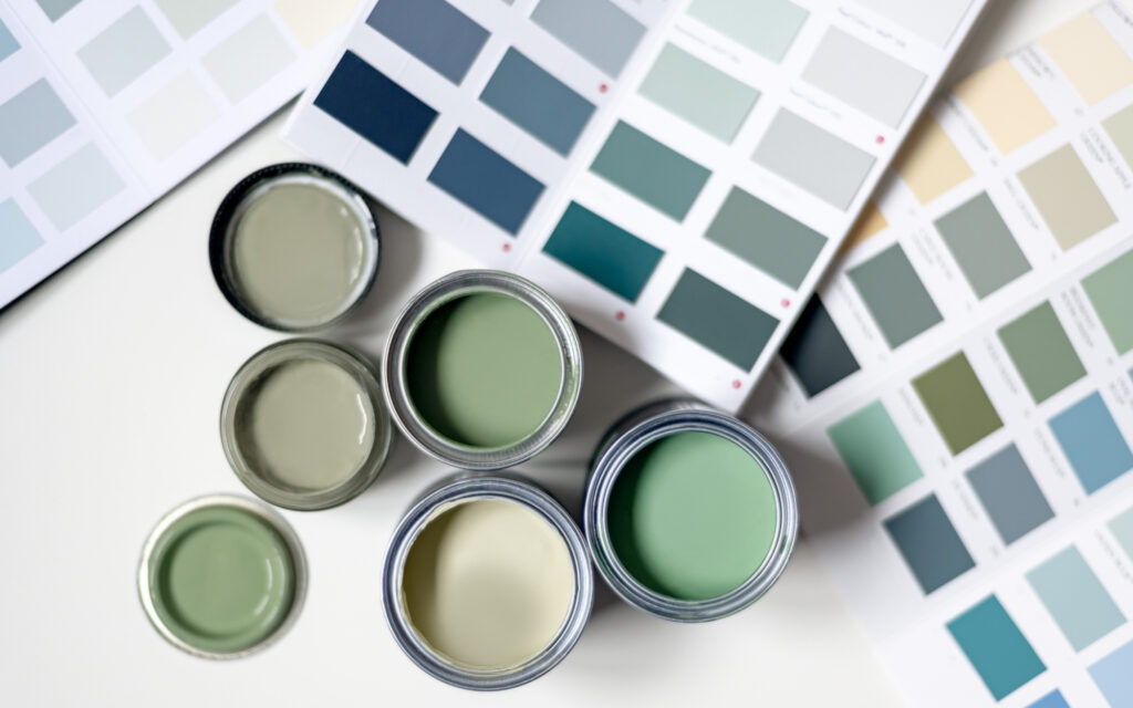 Five open cans of green paint in different shades and two sheets of paint color samples seen from above showing interior paint colors in minneapolis