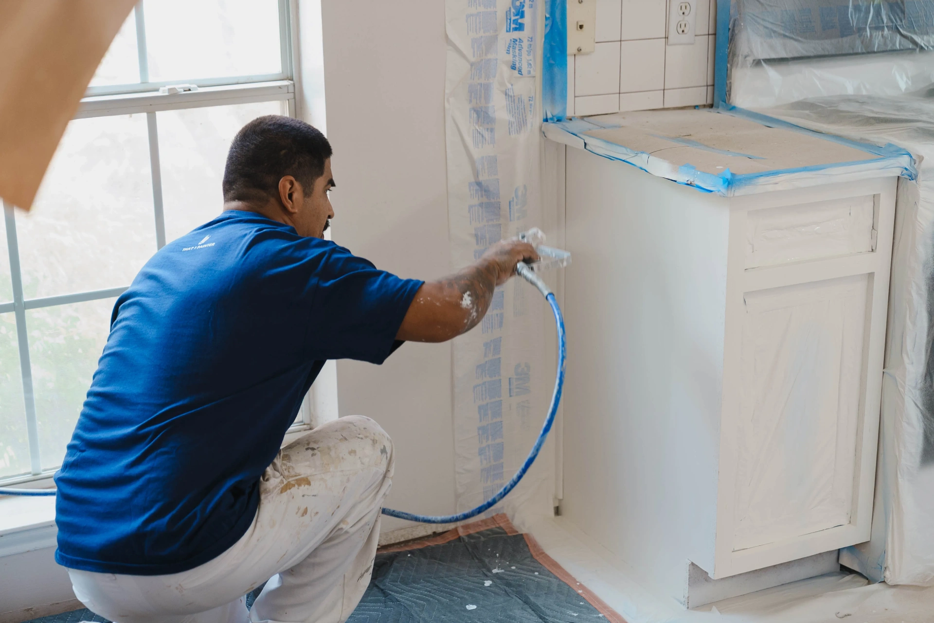 That 1 Painter crew member spraying base cabinet boxes near a window