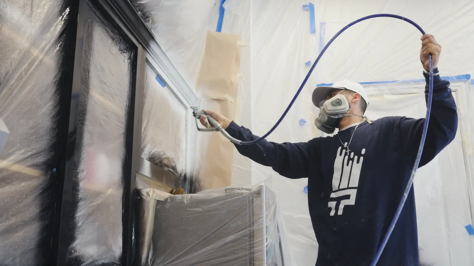 Painter spraying black finish on cabinetry inside a sealed spray booth