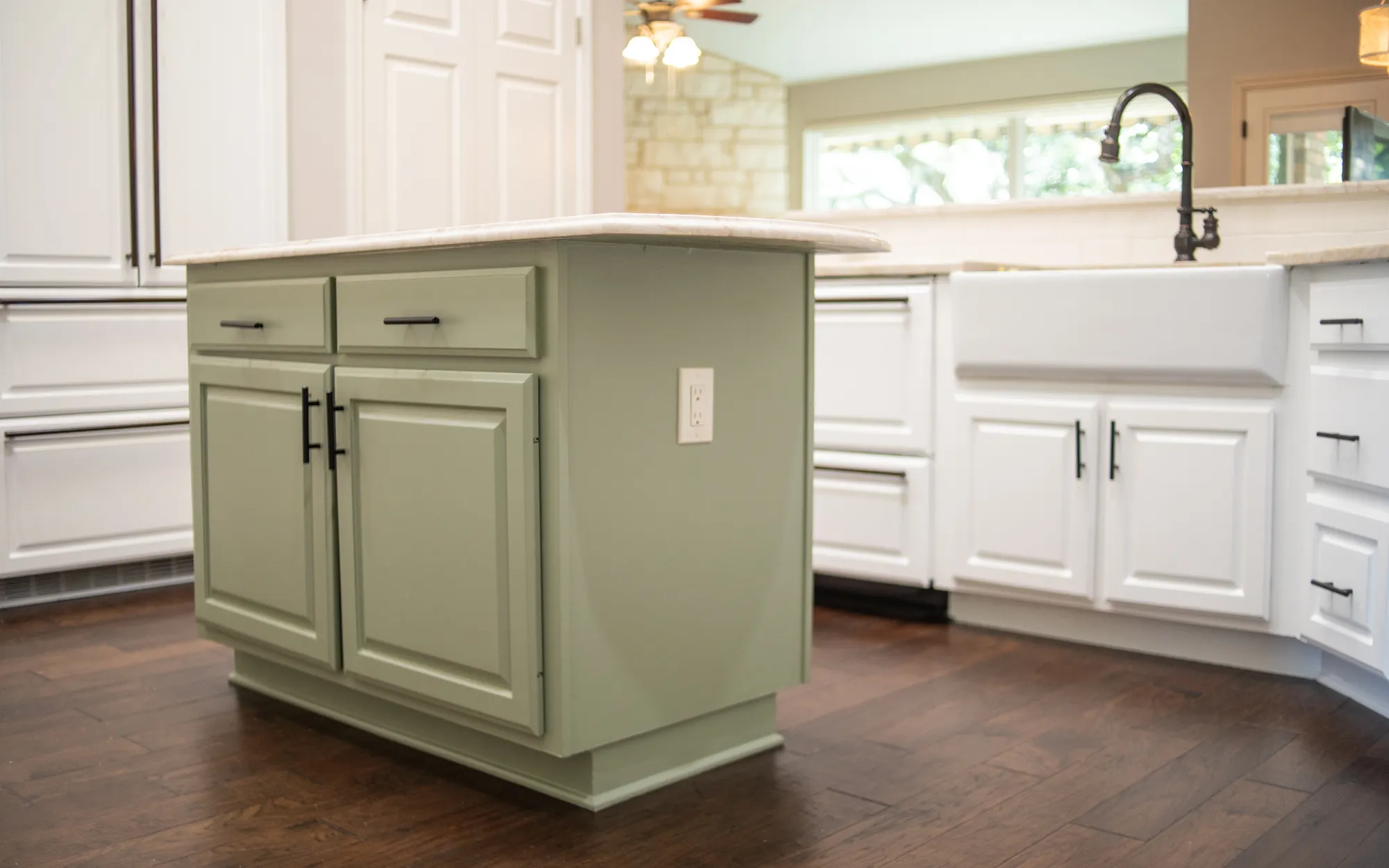 Sage green painted kitchen island with white perimeter cabinets and black hardware