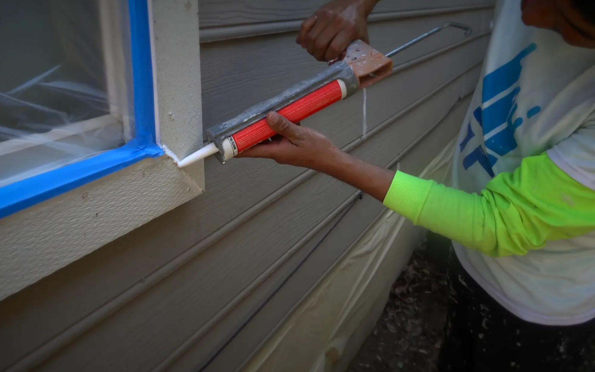 Caulk gun laying a clean bead along a taped exterior window casing