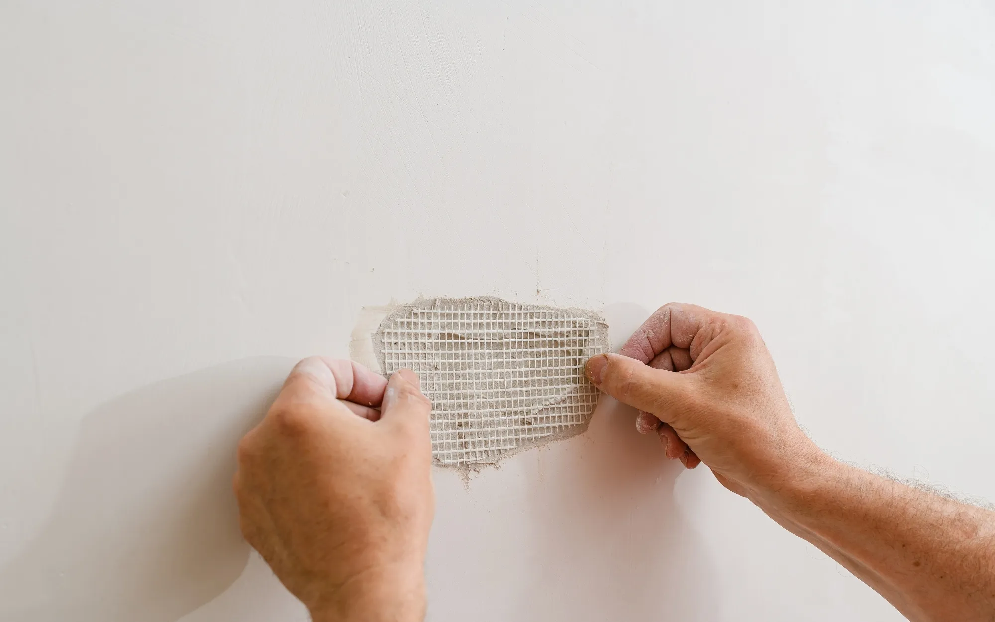 Drywall mesh patch being smoothed before priming and color-matched topcoat