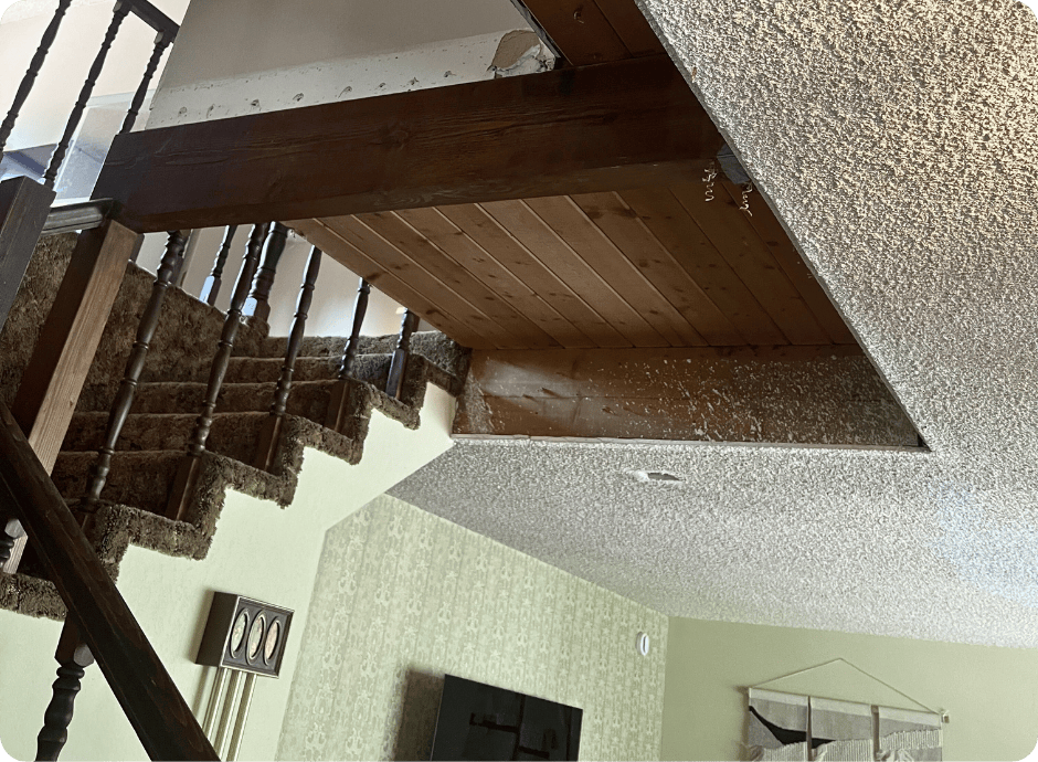 Cutout section in a popcorn ceiling exposing wooden beams above a staircase with that 1 painter