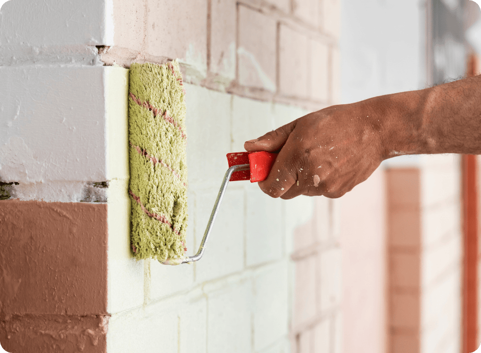Hand using a paint roller for brick painting, applying light green paint over an old multicolor brick wall that 1 painter