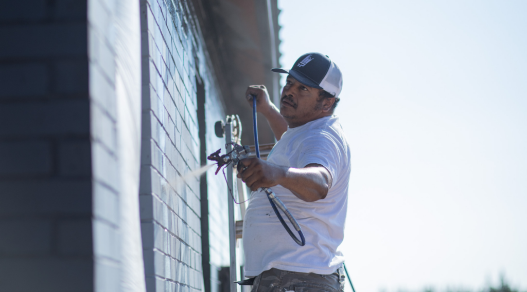 A painter painting exterior paint colors on a brick wall - That 1 Painter Dallas.