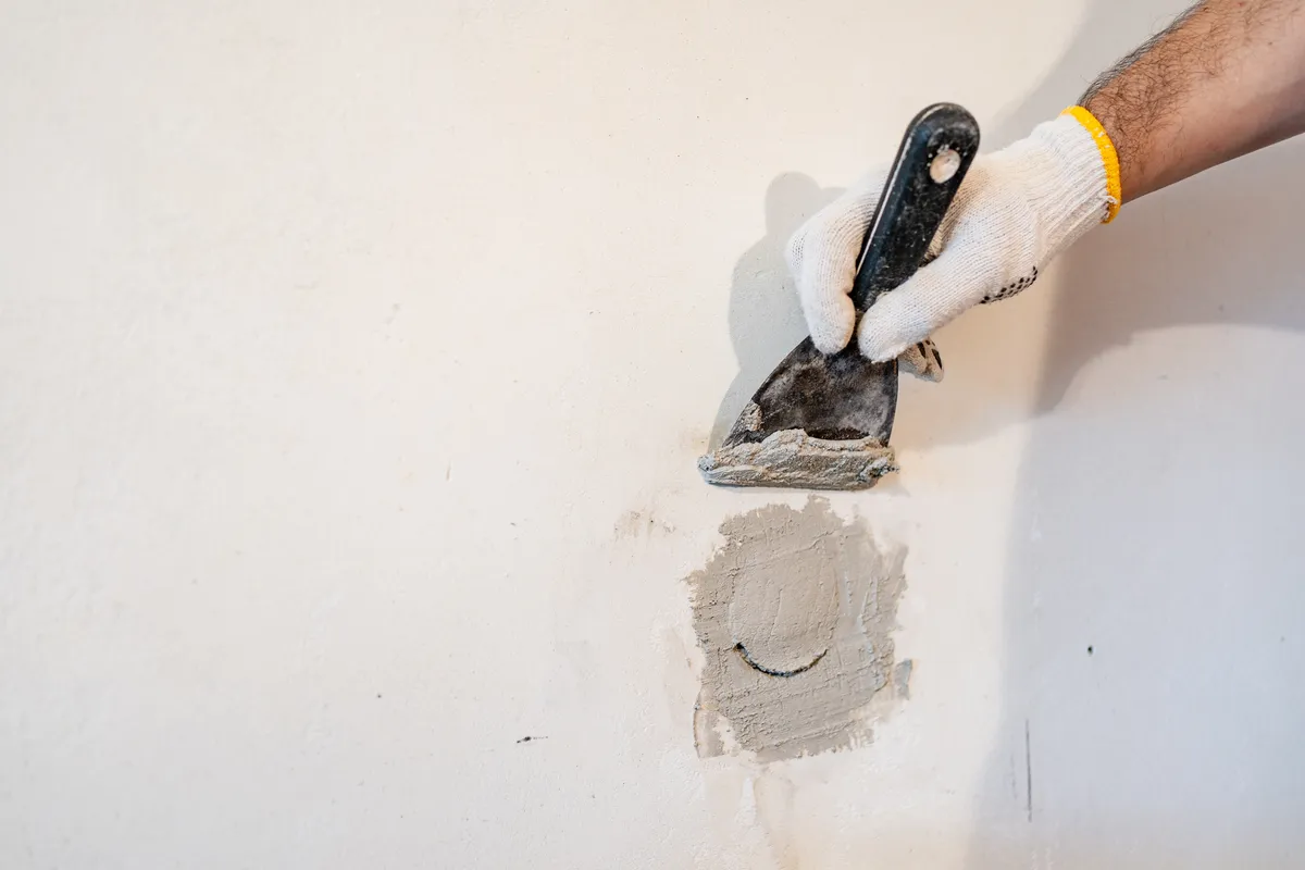 Gloved hand applying patching compound over a small hole in a white wall