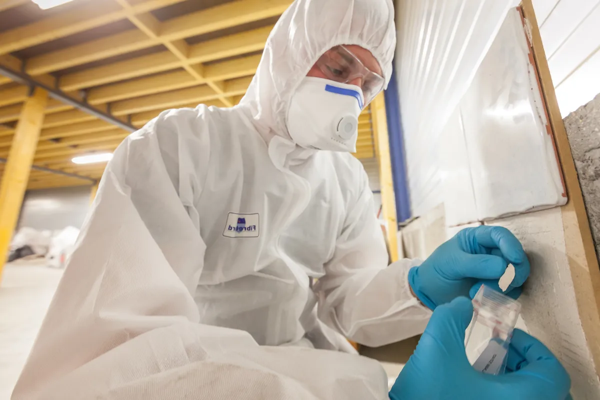 Asbestos surveyor in protective gear sealing a building material sample in a bag