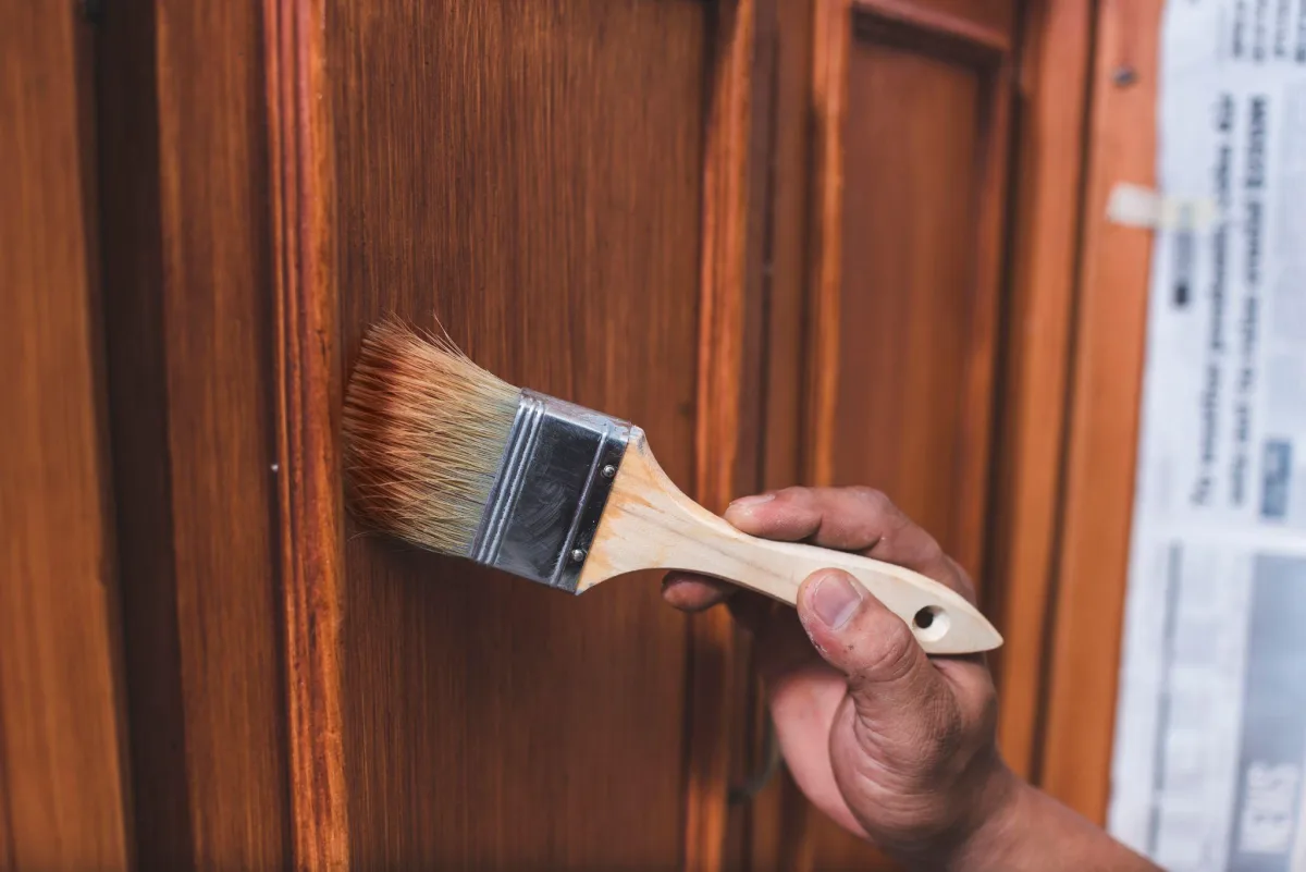 Hand brushing a coat of finish onto a wood kitchen cabinet door