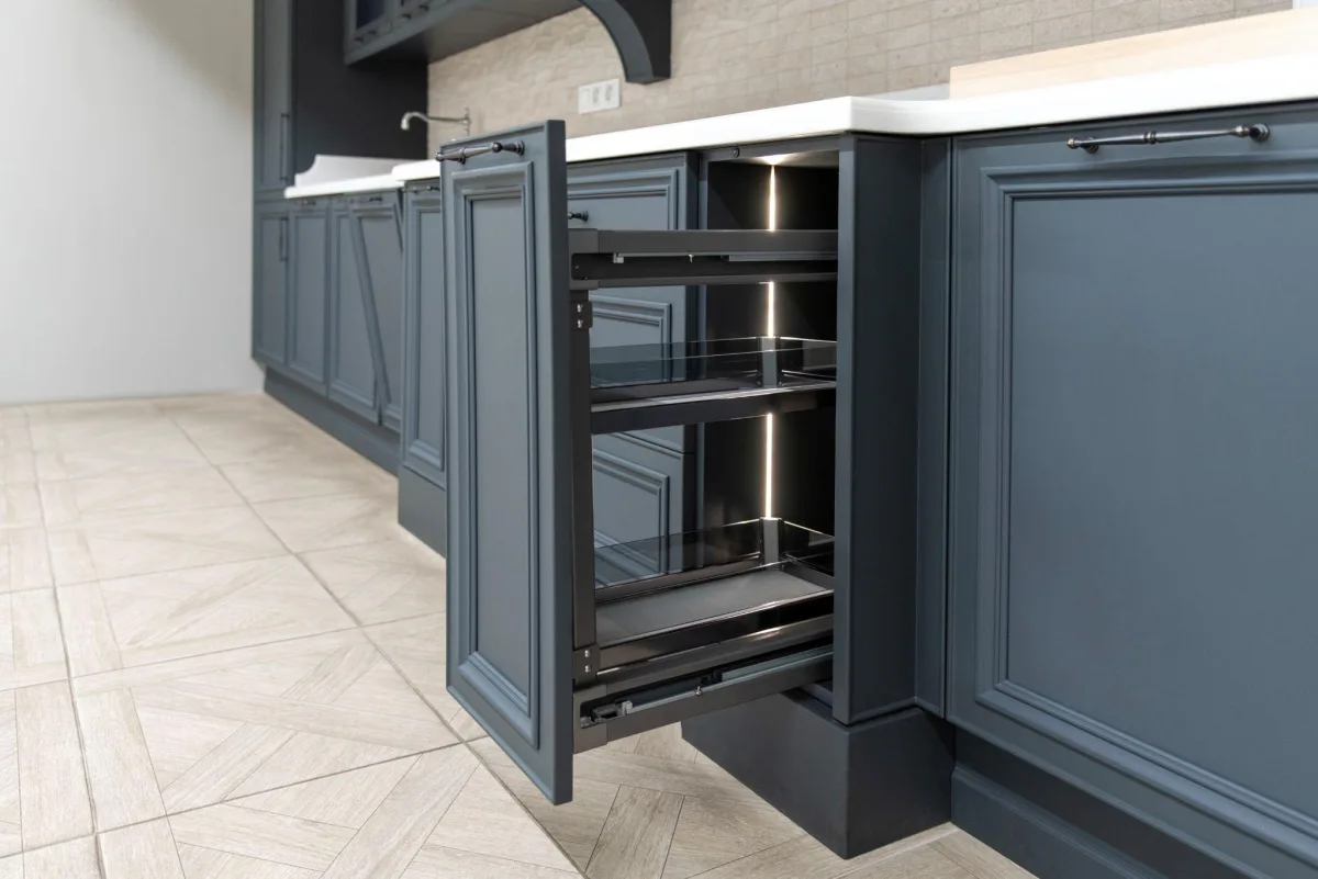 Slate blue painted kitchen base cabinets with a lit pull-out pantry drawer open