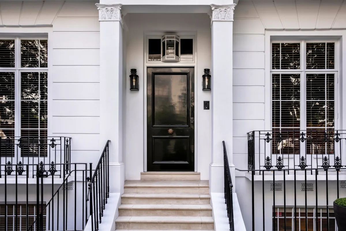 Glossy black front door framed by white columns and a white painted entry with black iron railings