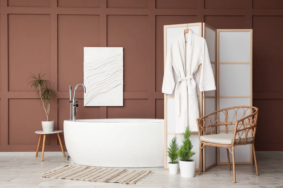 Bathroom with a brown painted paneled wall, white bathtub, robe and folding screen