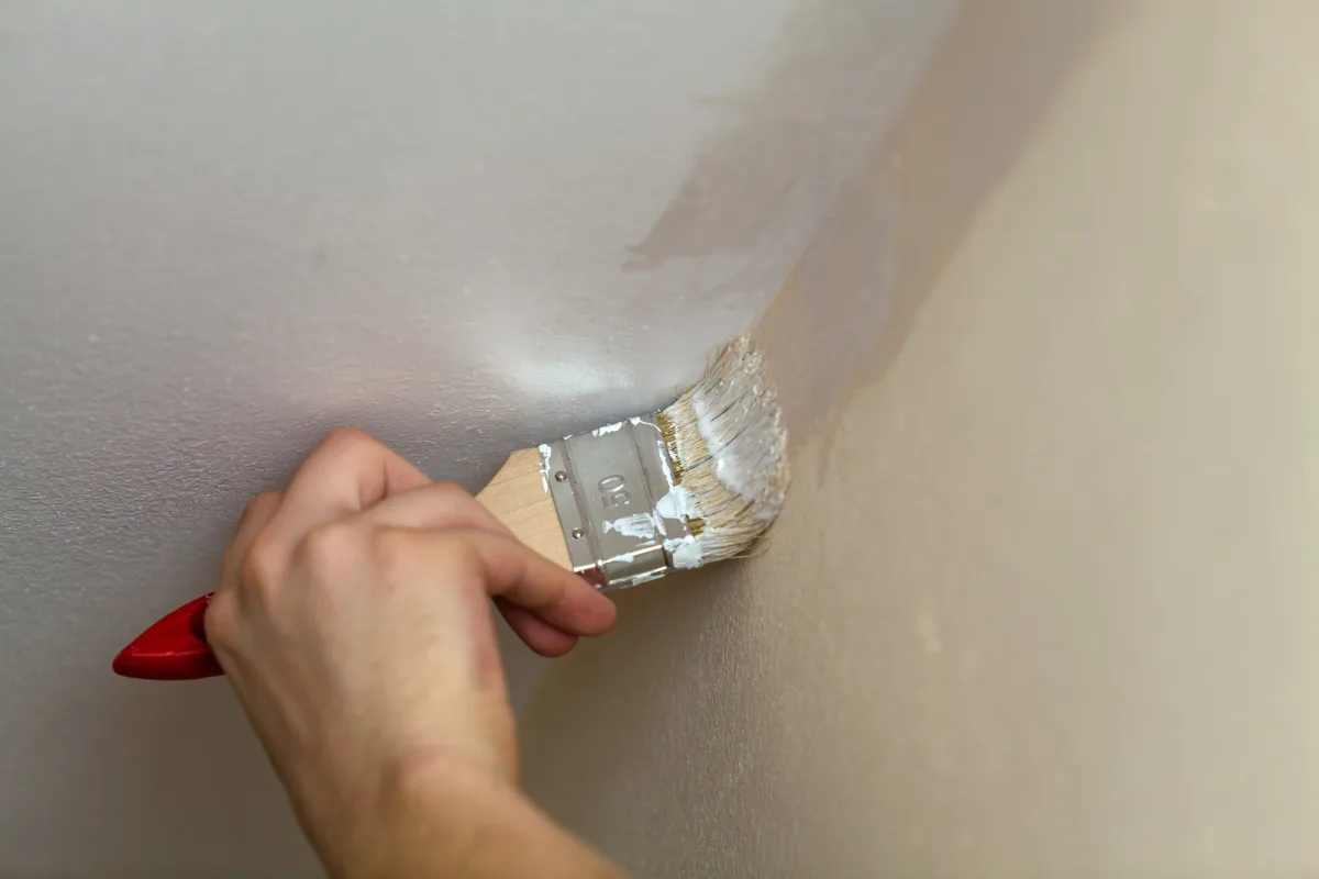 Hand cutting in white paint along a ceiling edge with a flat brush