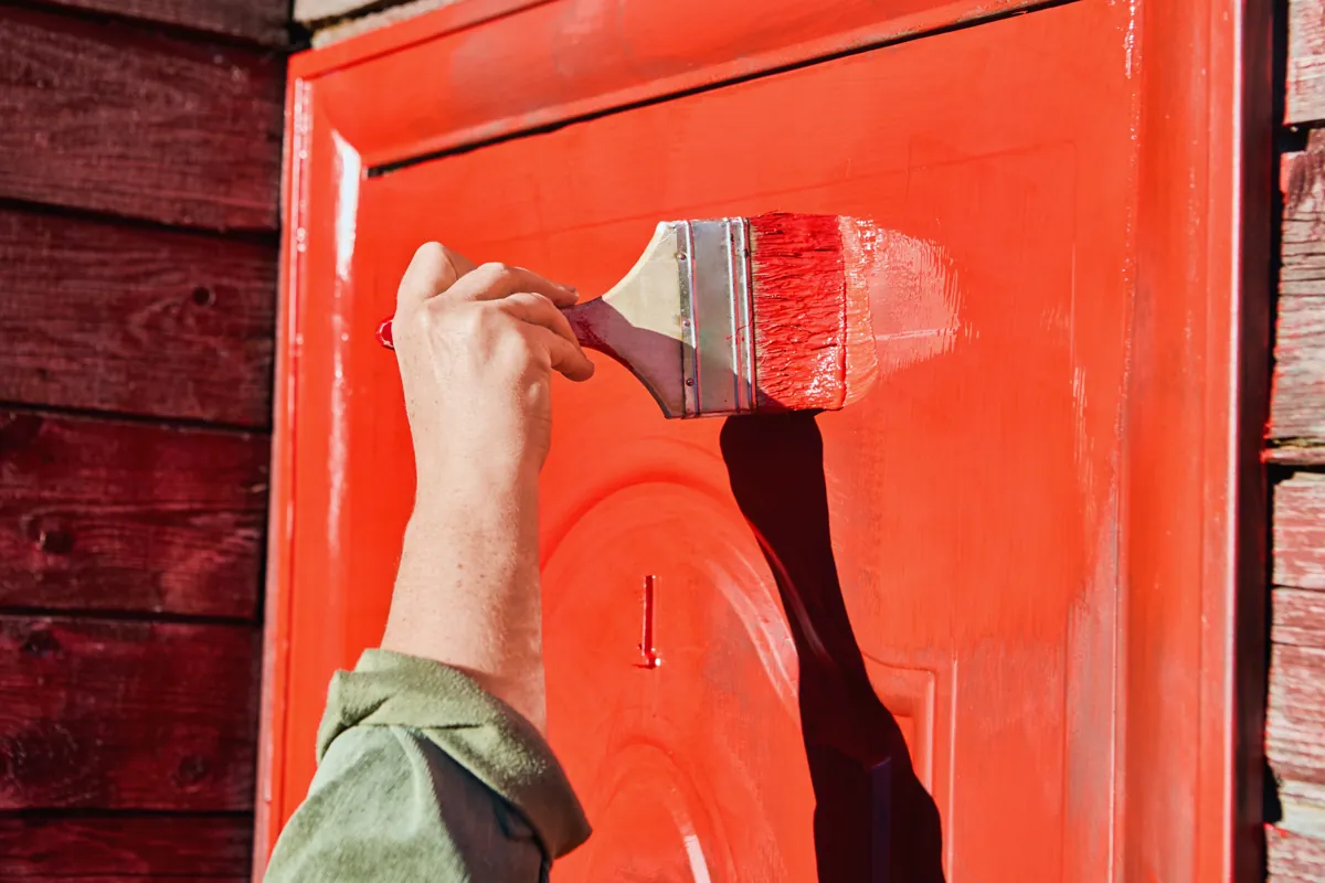 Hand brushing red paint onto the panels of a metal entry door