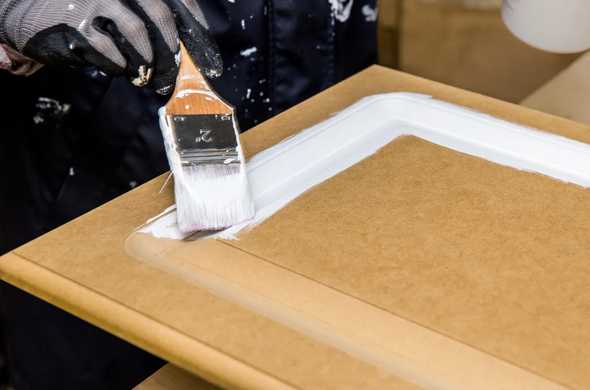 Brush applying white enamel paint to the edge of a cabinet door