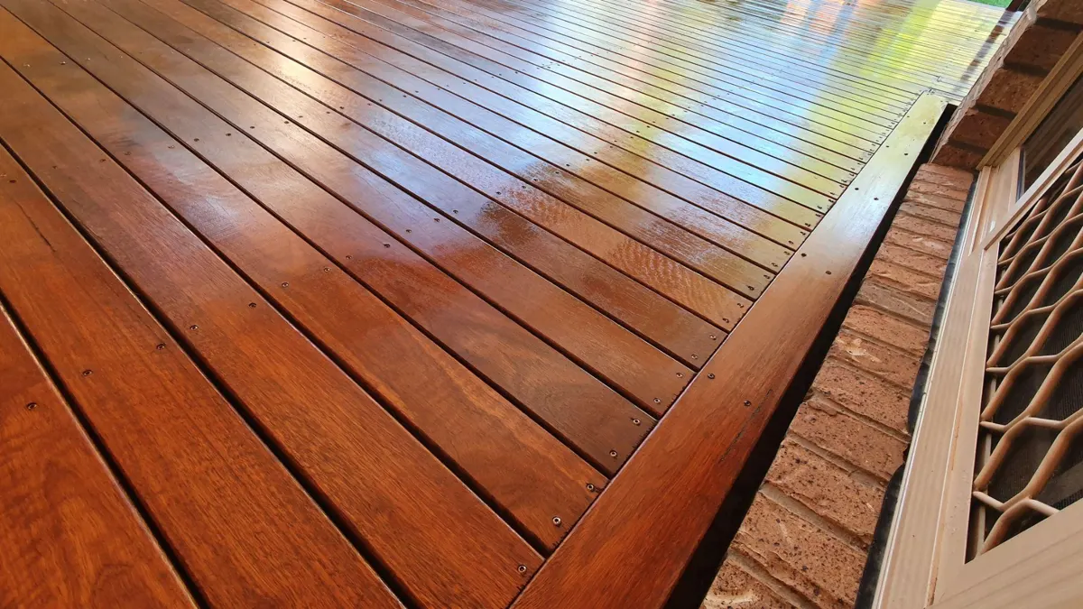 Close-up of a wet, freshly stained hardwood deck with screwed boards along a brick wall