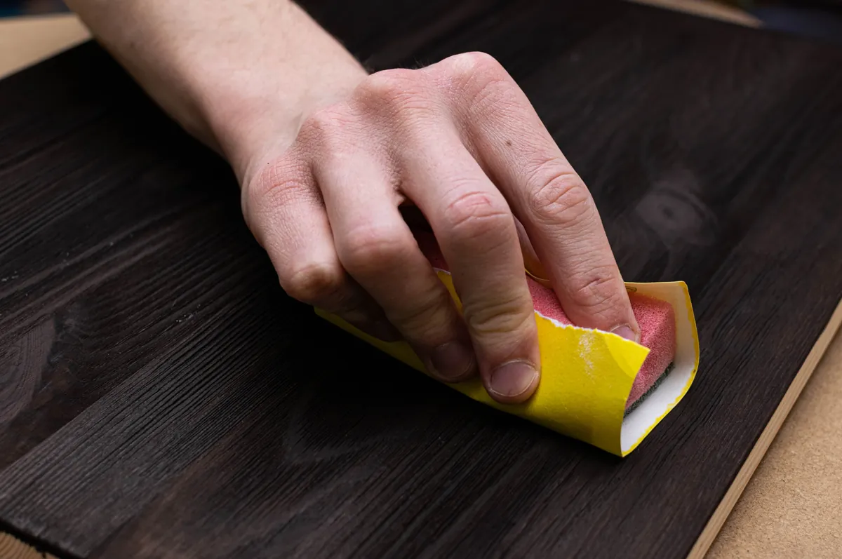 Hand sanding a dark wood surface with a folded sheet of sandpaper