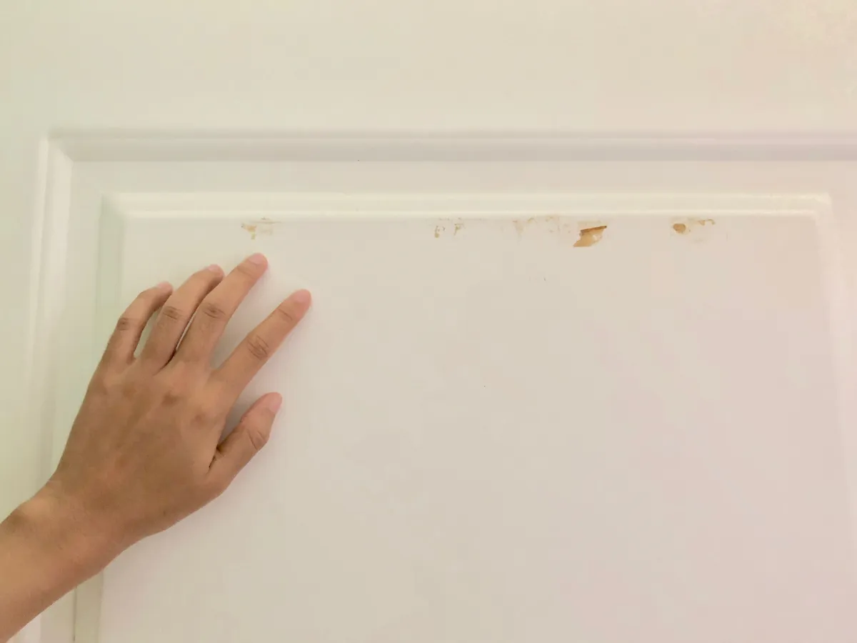 Hand touching a white painted door panel to test whether the paint is dry