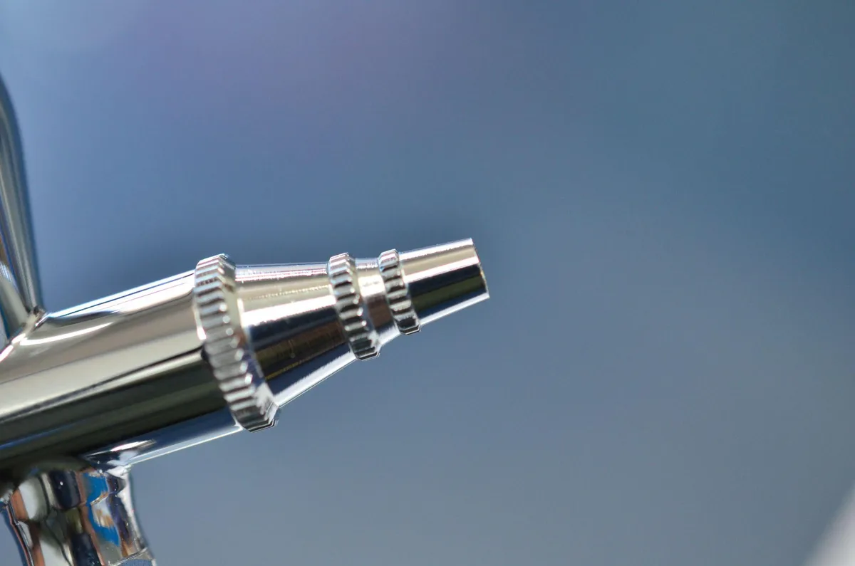 Close-up of a chrome spray gun nozzle against a blue background