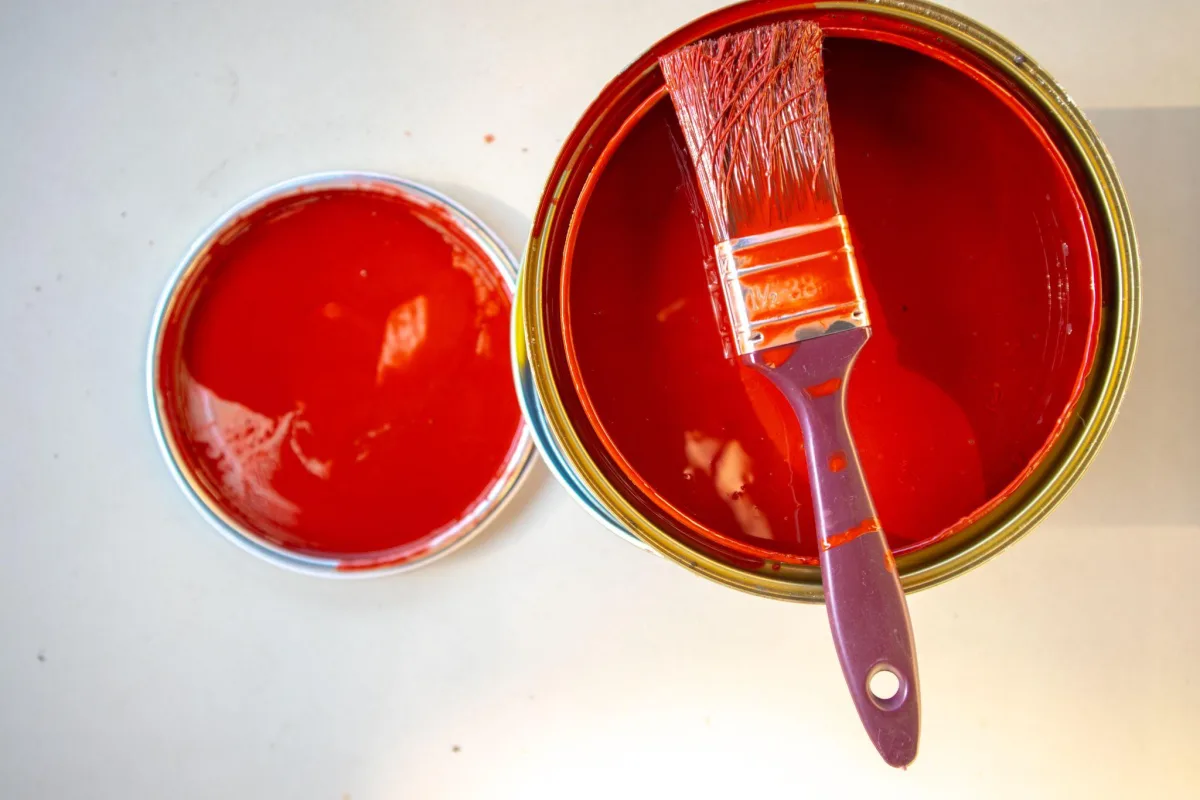 Open can of red paint with a brush resting across the rim