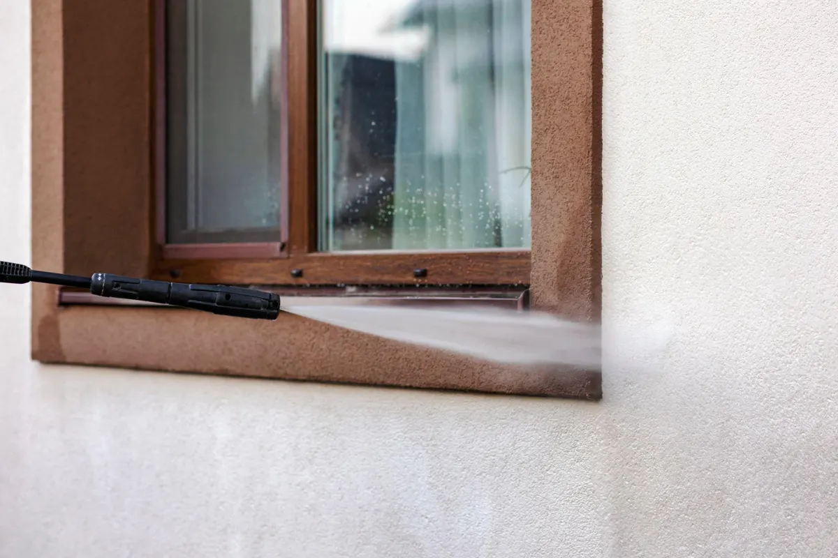 Pressure washer wand spraying the stucco trim below an exterior window