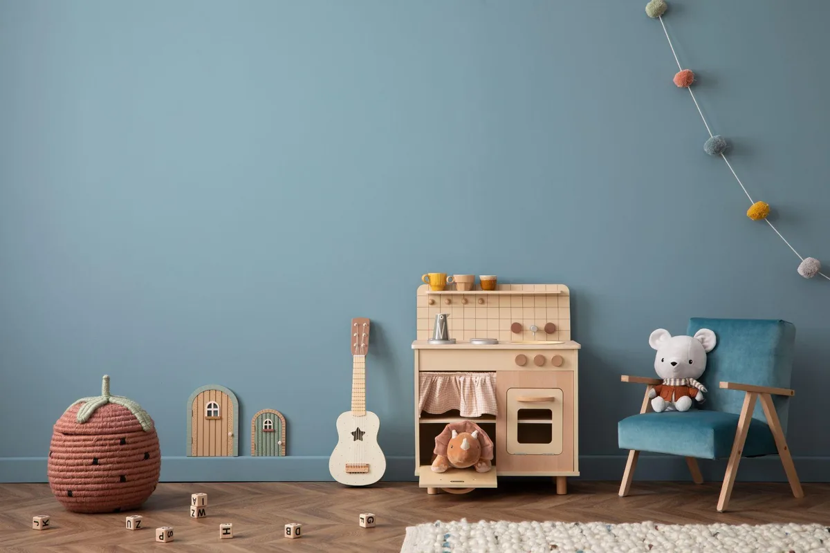Kids playroom with a dusty blue painted wall, wooden play kitchen, ukulele, and a small blue armchair