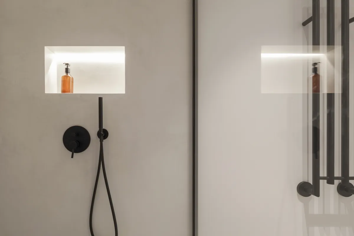 Walk-in shower with smooth gray microcement-style walls, a lit niche and black fixtures