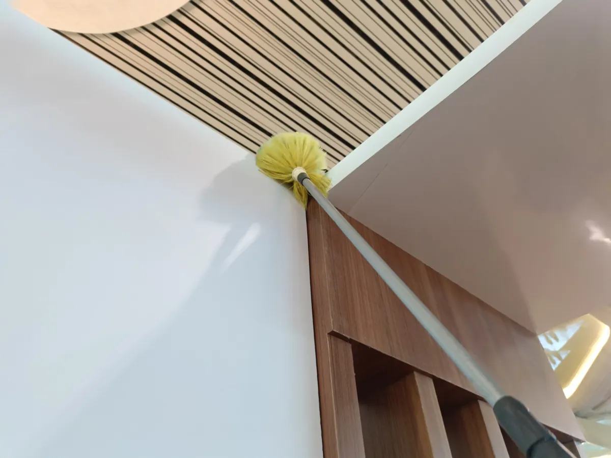 Microfiber duster on a telescopic pole cleaning a ceiling corner