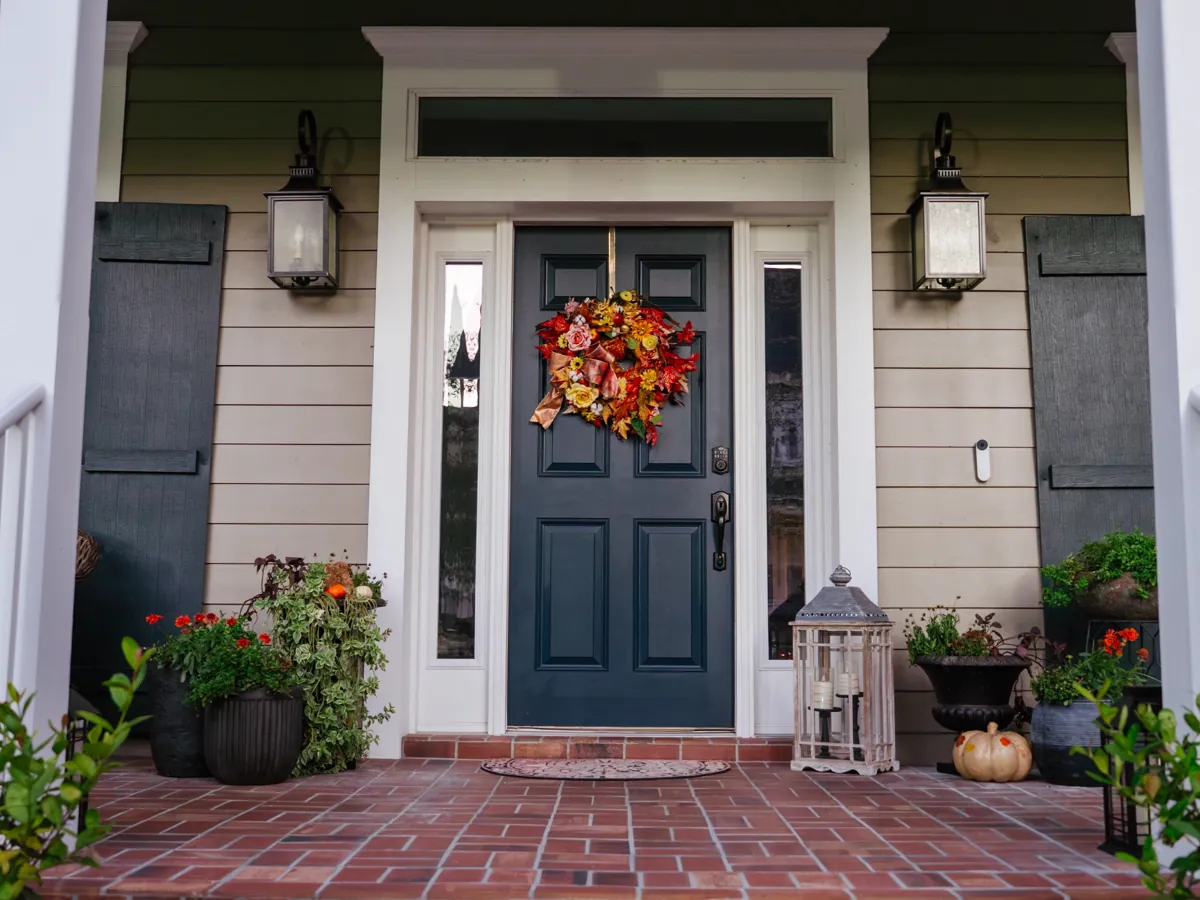 Navy blue front door with a colorful autumn wreath, black shutters and a brick walkway