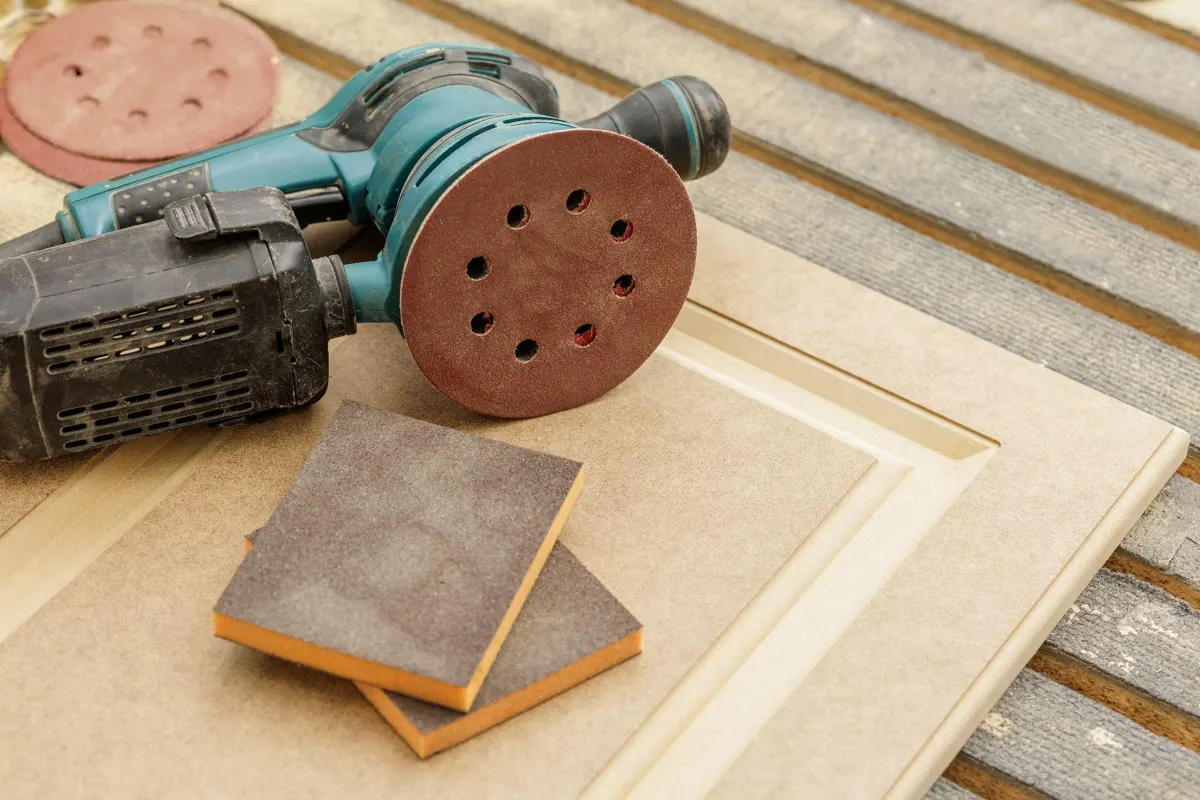 Random orbital sander and two sanding sponges resting on an unpainted cabinet door