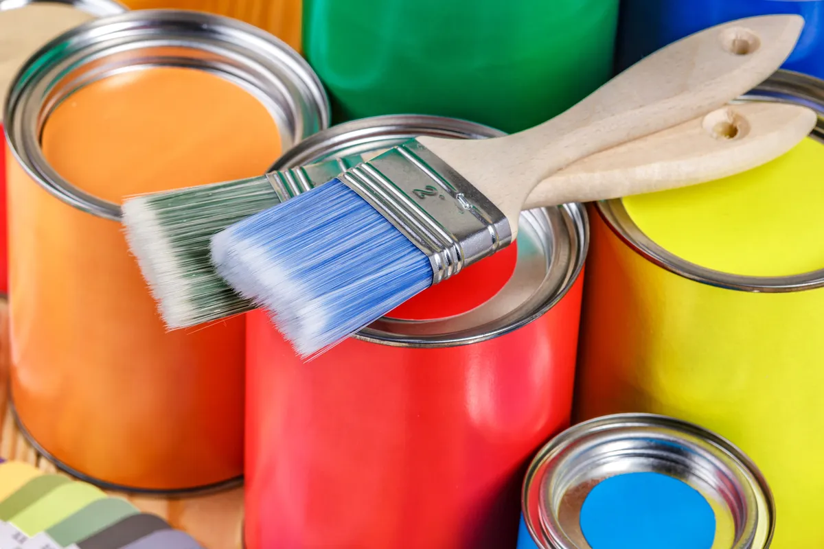 Open cans of orange, red, yellow and blue paint with paint brushes resting on top