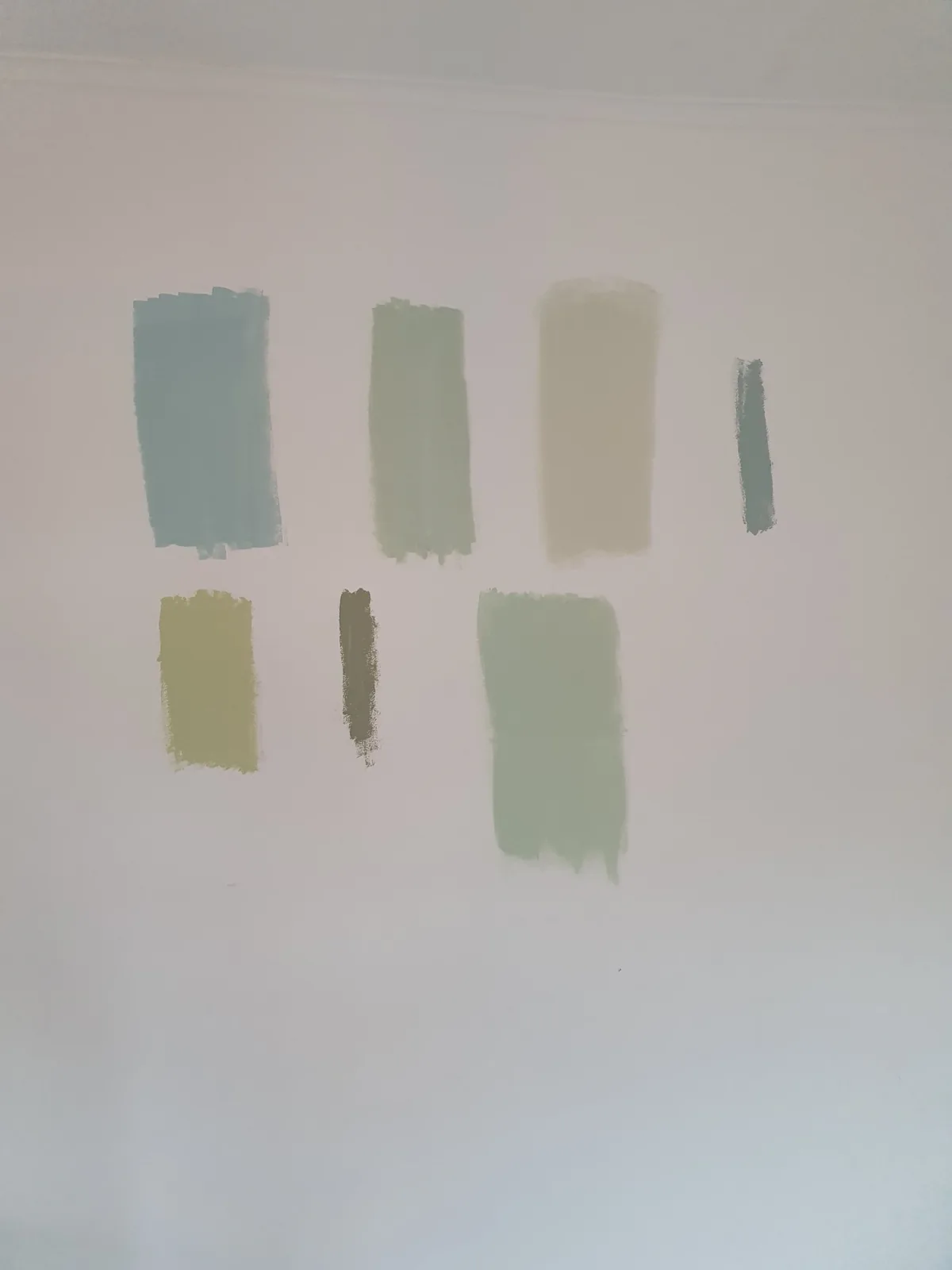 Green and blue-gray paint sample swatches brushed onto a white wall