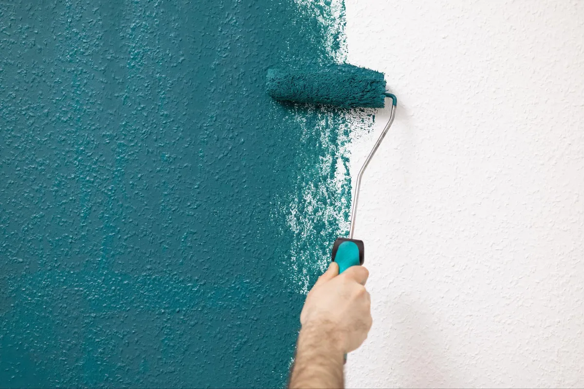 Hand rolling teal paint over a white orange peel textured wall with a paint roller