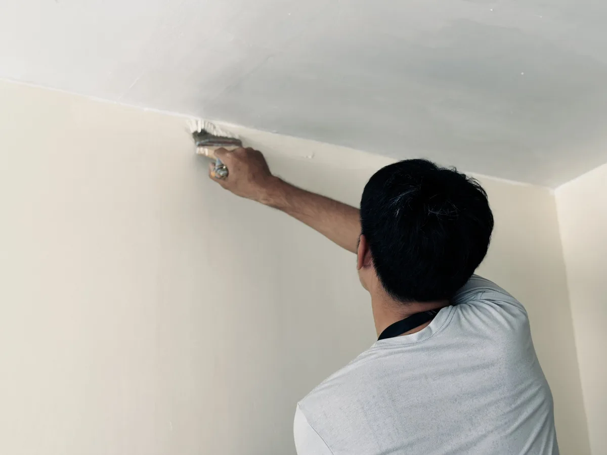 Painter cutting in with a brush along the ceiling line of a cream bedroom wall