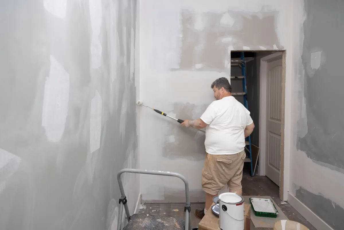 Painter rolling primer over patched drywall in a bedroom being prepared for paint