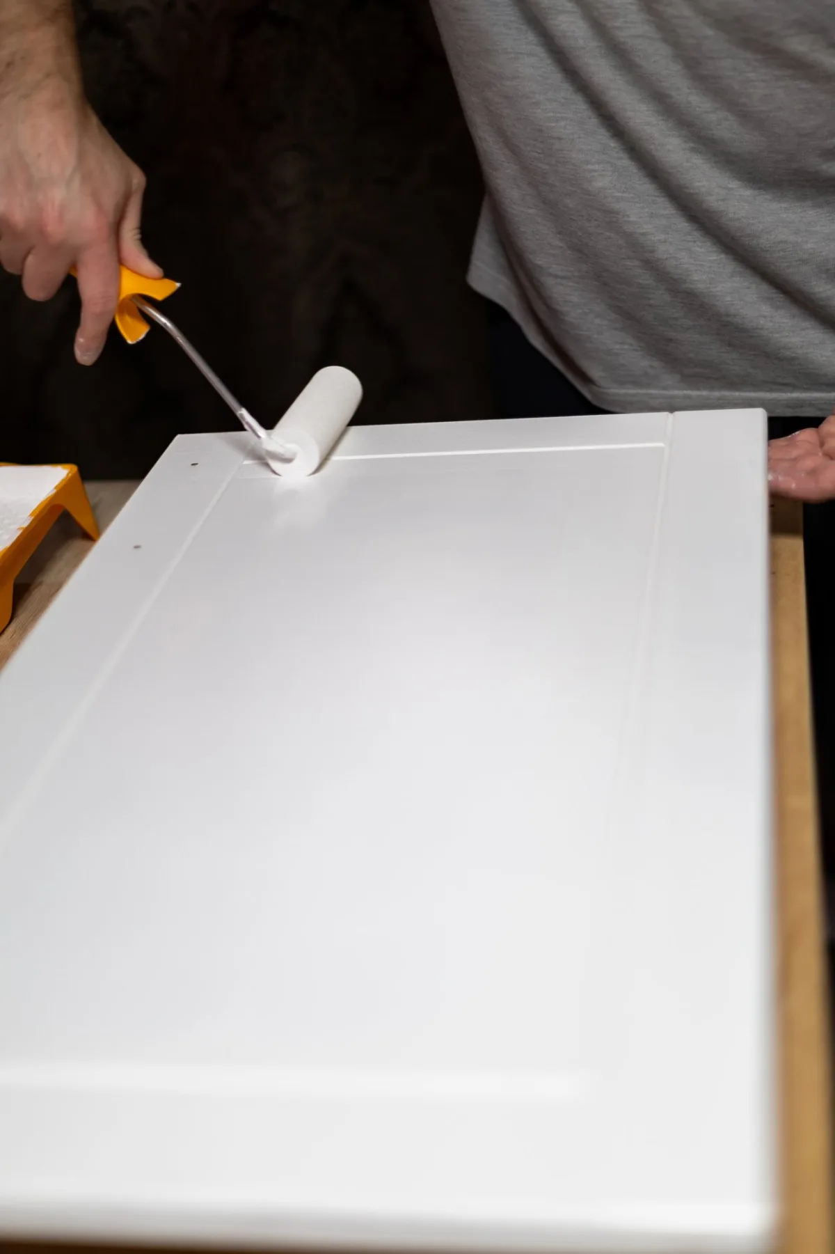 Painter rolling white paint onto a shaker-style cabinet door laid flat