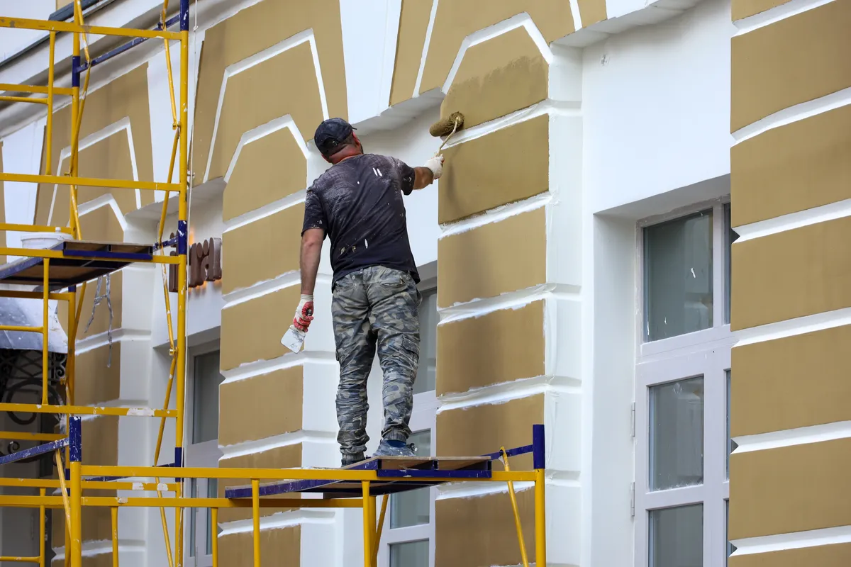 Painter on scaffolding painting a masonry house facade