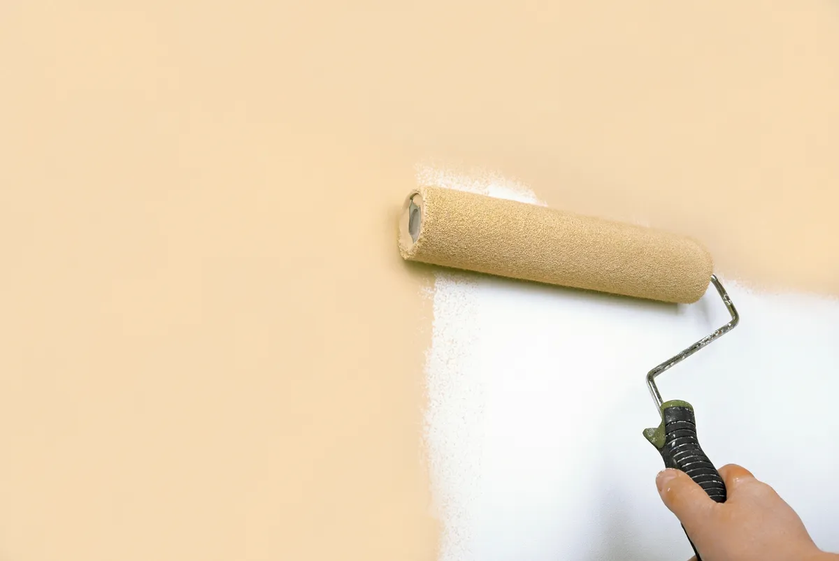 Paint roller applying a warm beige color over a white wall