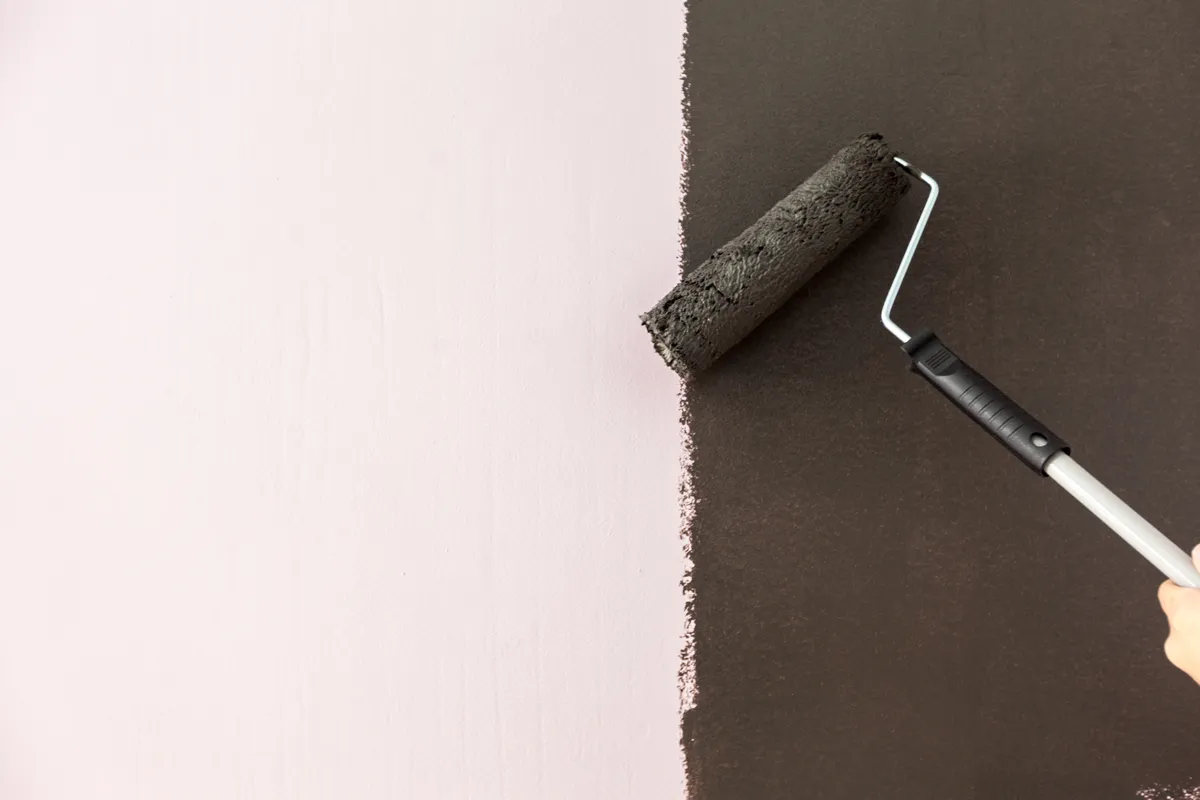 Paint roller covering a light wall with dark charcoal paint