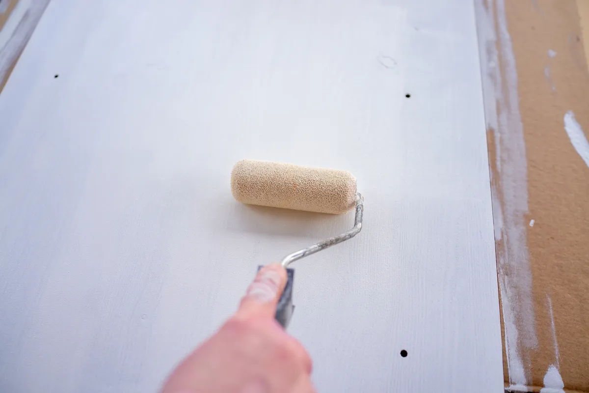 Hand rolling white primer over a wall with patched holes