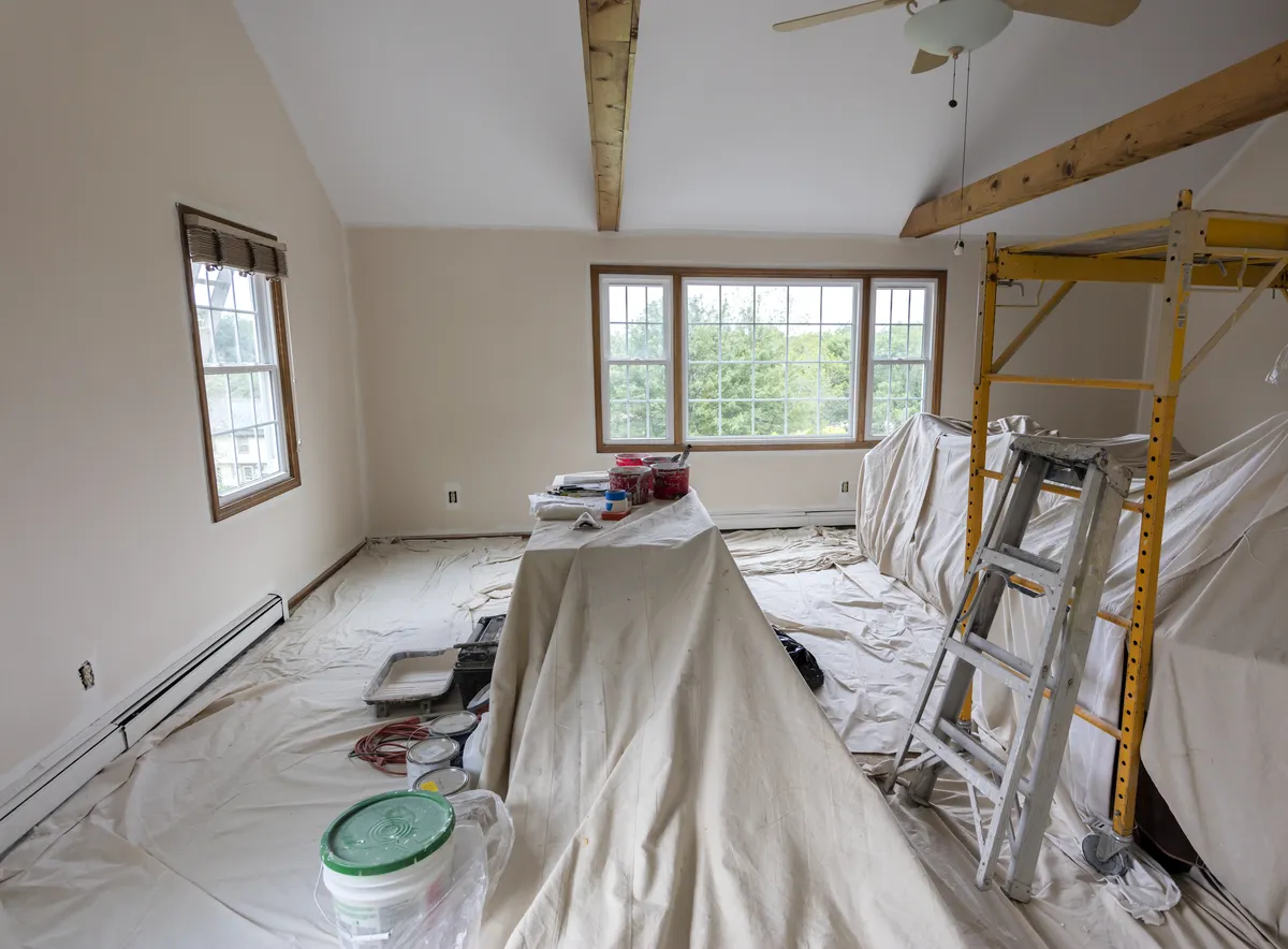 Room covered in drop cloths with a ladder and paint buckets during painting