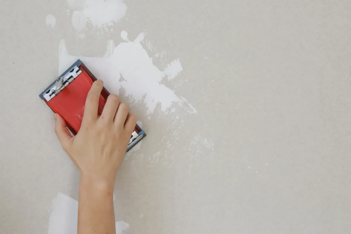 Hand sanding a patched wall smooth with a red sanding block