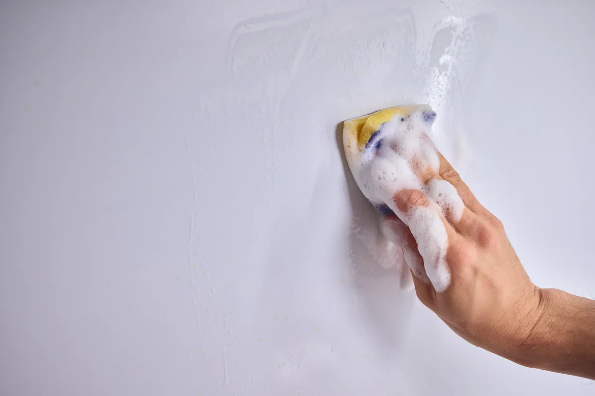 Hand wiping a scuff off a painted interior wall with a soapy sponge