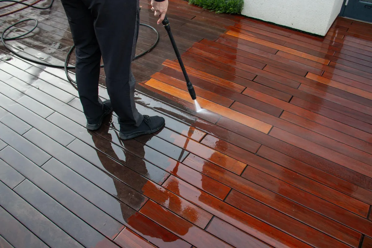 Person pressure washing dark hardwood deck boards before staining