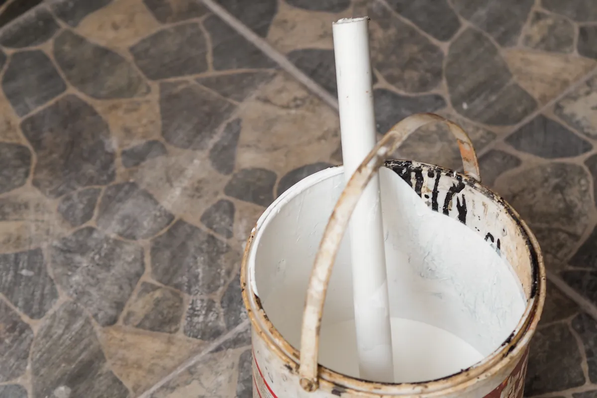 Stir stick standing in an open can of white paint on a stone floor