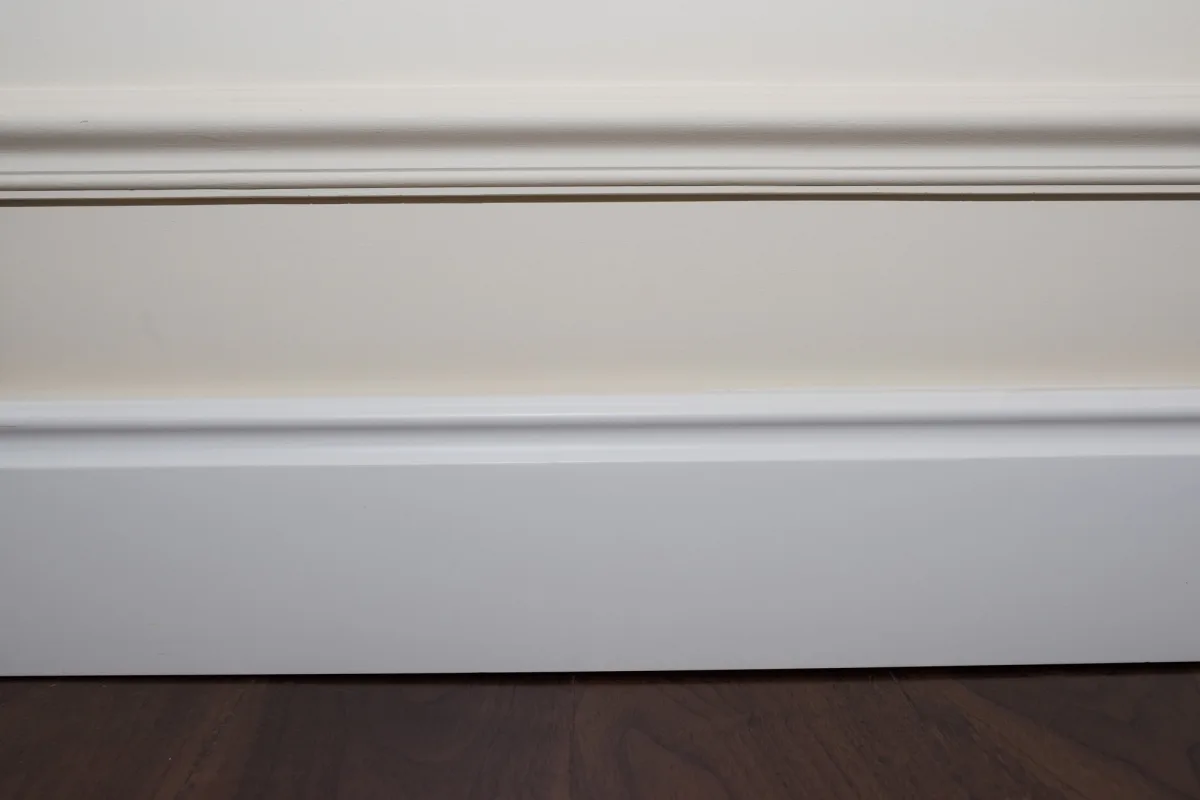 Close-up of white baseboard and molding against a cream painted wall above a dark wood floor