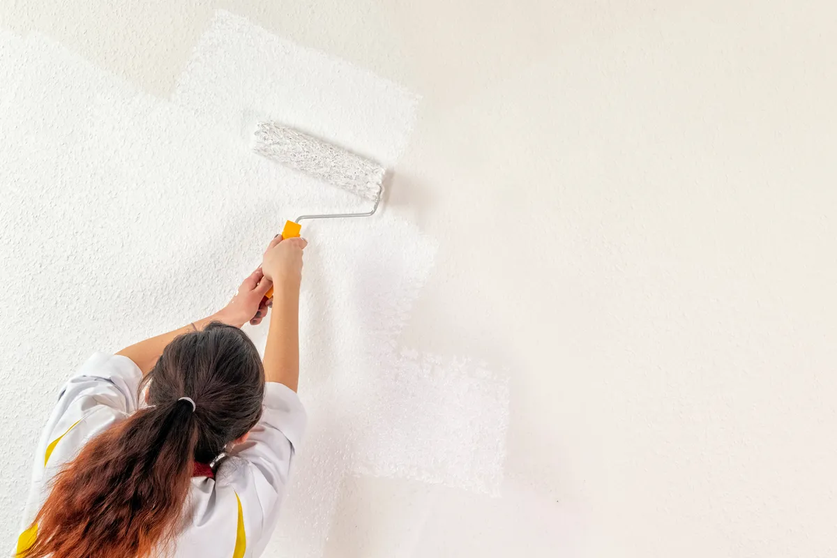 Woman rolling white paint onto an interior wall