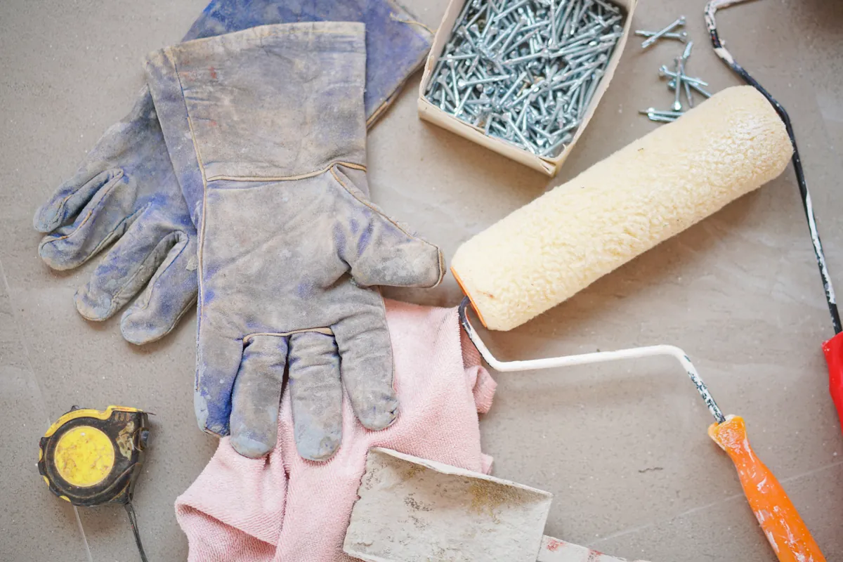 Worn work gloves, rags, screws and a paint roller laid out on a workbench