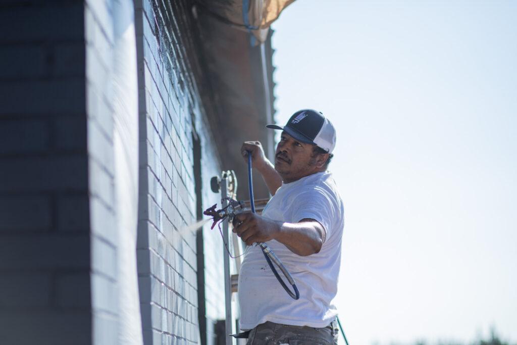 A painter spray painting the exterior of a commercial building with black paint - That 1 Painter Knoxville