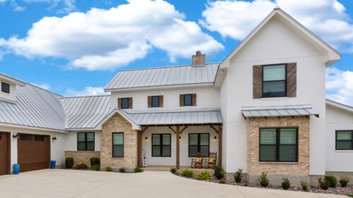 Large house with tan brick, natural wood porch posts, and white stucco painted by professional painters in Mustang.